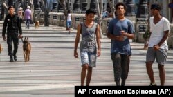 Jóvenes caminan por el Paseo del Prado mientras miembros de la policía patrullan en La Habana, el 11 de julio de 2022. (AP Foto/Ramon Espinosa)