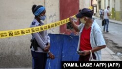 Una oficial de policía exige identificación a un ciudadano en una calle de La Habana cerrada por coronavirus. (YAMIL LAGE / AFP)