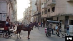 Un carretón con un caballo y un bicitaxi circulan por una calle de La Habana, Cuba.